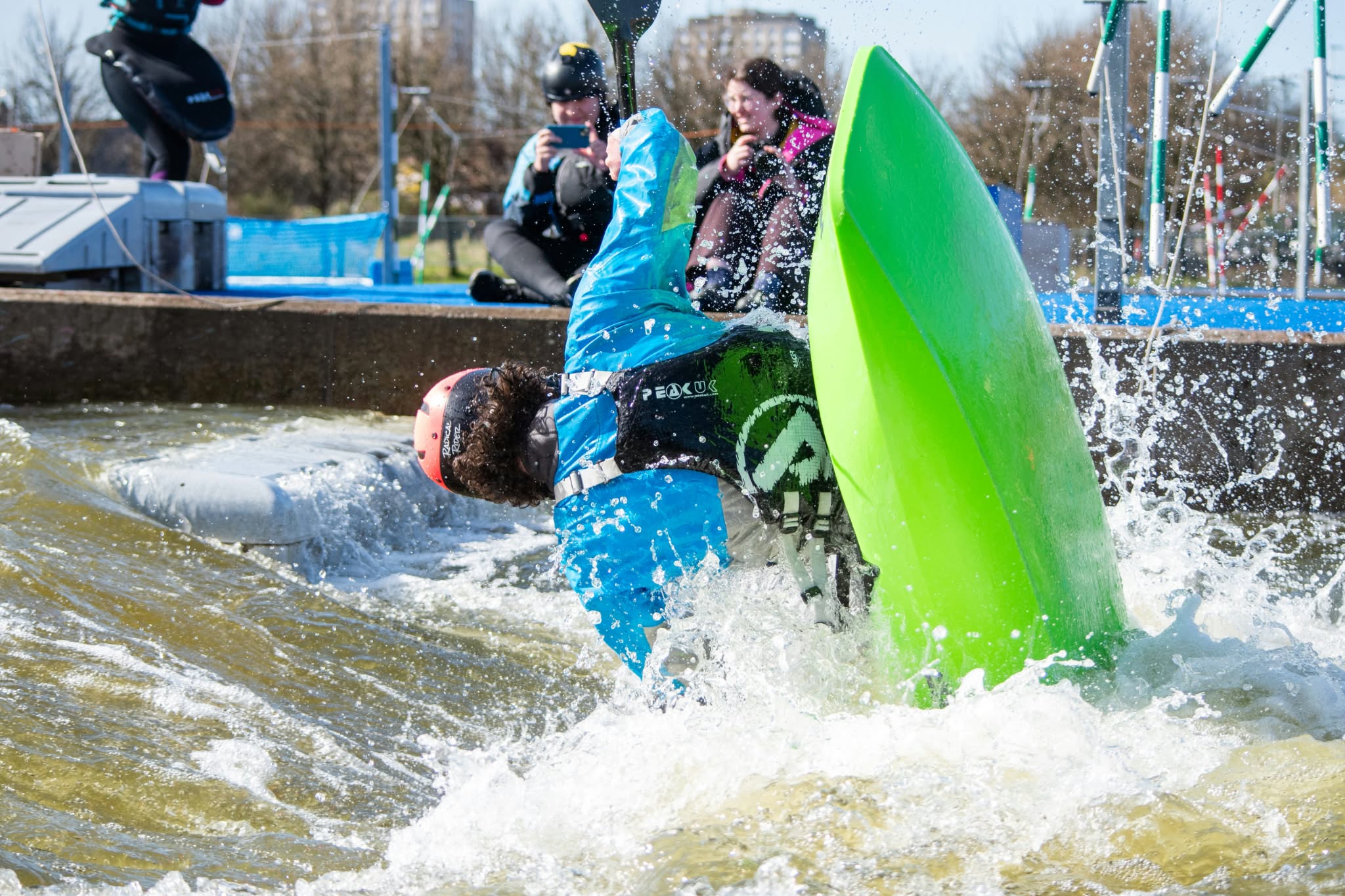 Freestyle kayaker performing a vertical move in a green boat at Pinkston Watersports in Glasgow